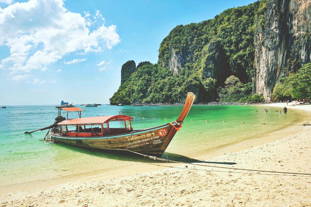 Longtailboot am Strand von Krabi mit türkisfarbenem Meer und Kalksteinfelsen im Hintergrund  in Thailand