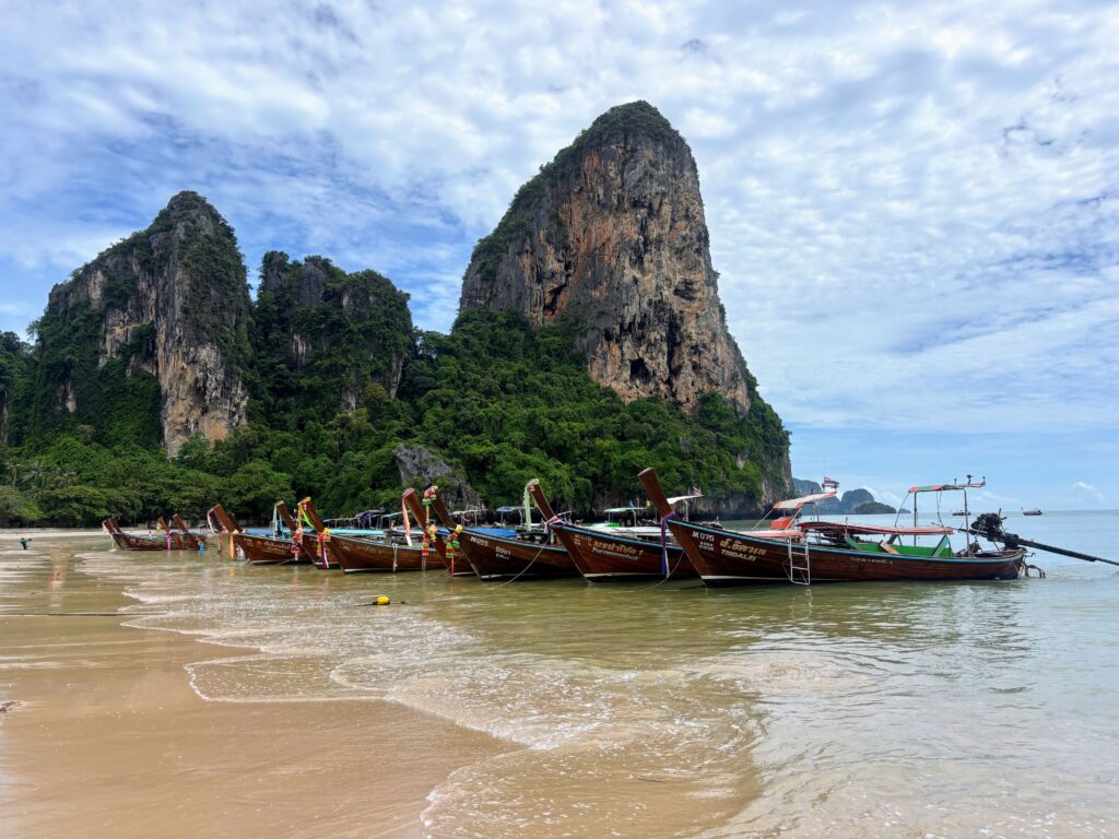 Railay Beach in Krabi mit Longtail-Booten vor bewachsenen Kalksteinfelsen